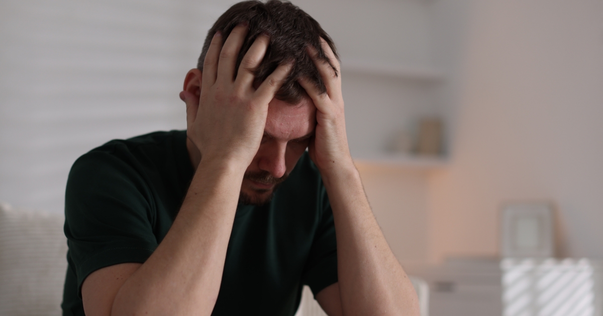 Man indoors, hands on his head, looking stressed or overwhelmed in a calm living room setting.