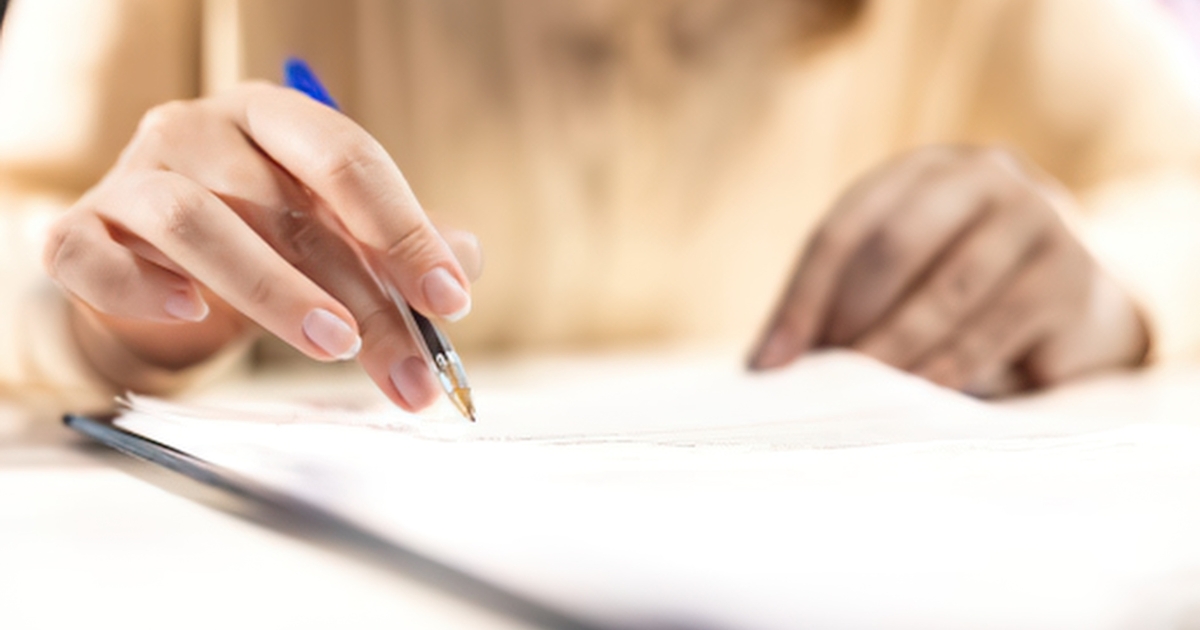 Close-up of a hand writing with a blue pen on white paper at a desk